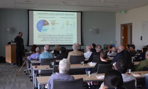 人 sit in a room watching a presentation on renewable electricity. 