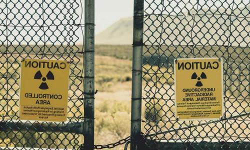 Fence with radiation warning signs 和 desert l和scape in background