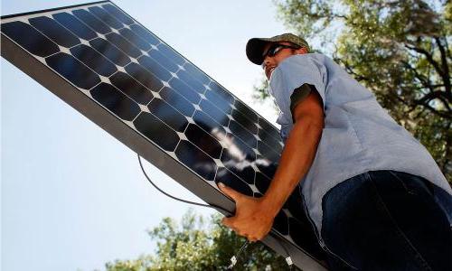 Person with hat and glasses hoisting up a solar panel